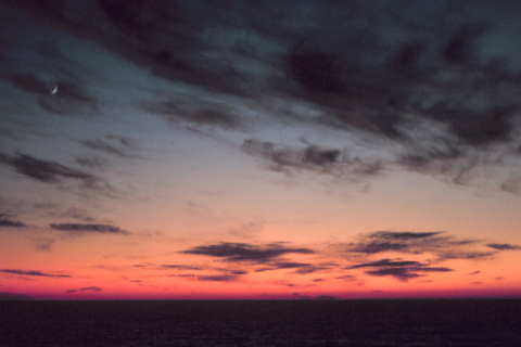 Ein gebogener, schwarzer Horizont, unten dunkelrot, darüber heller werdend, und ein paar leicht Wolken am Himmel