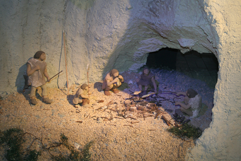 Im bräunlich-sandfarbenen Modell einer Höhle sind Figuren mehrerer Urmenschen zu sehen